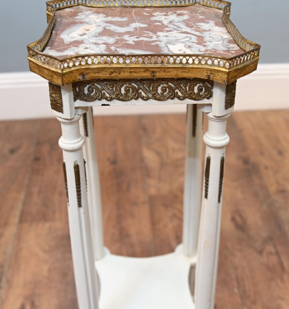 A white painted tall French pedestal stand featuring four fluted legs, gilt brass mounts, a lower tier, and a shaped variegated marble top with a brass gallery. View III