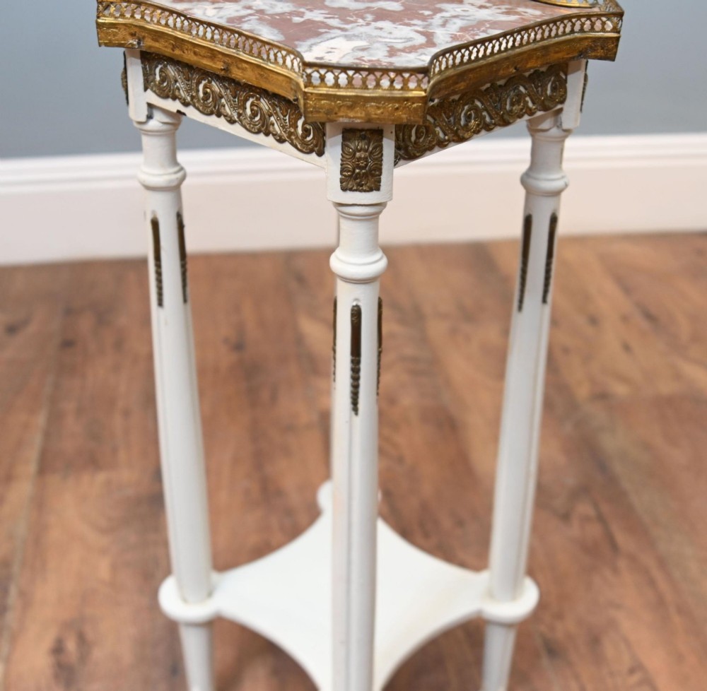 A white painted tall French pedestal stand featuring four fluted legs, gilt brass mounts, a lower tier, and a shaped variegated marble top with a brass gallery. View V