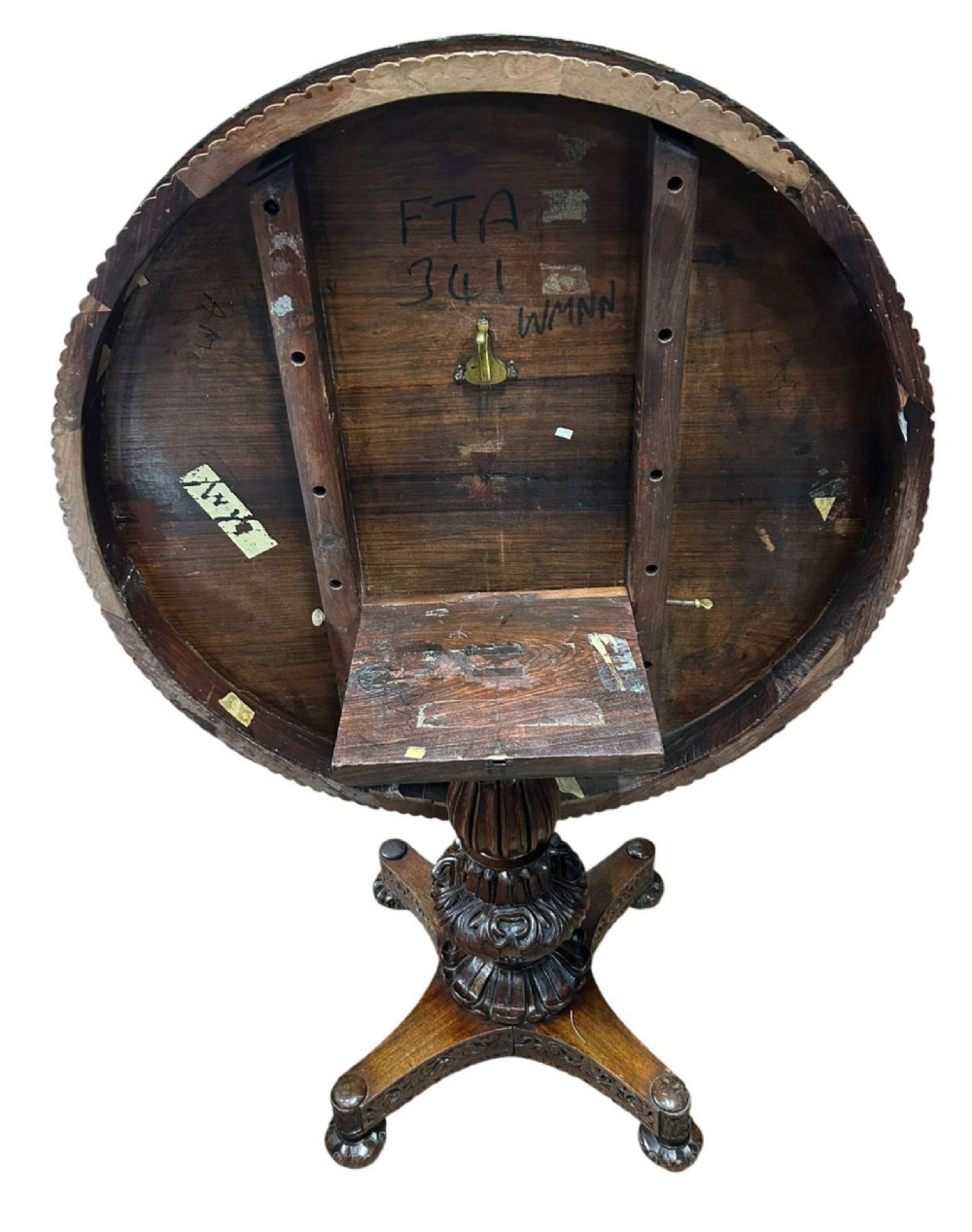 A round antique Burmese hardwood dining table featuring a polished top, an intricately carved apron, and a central pedestal base with tripod legs. View V