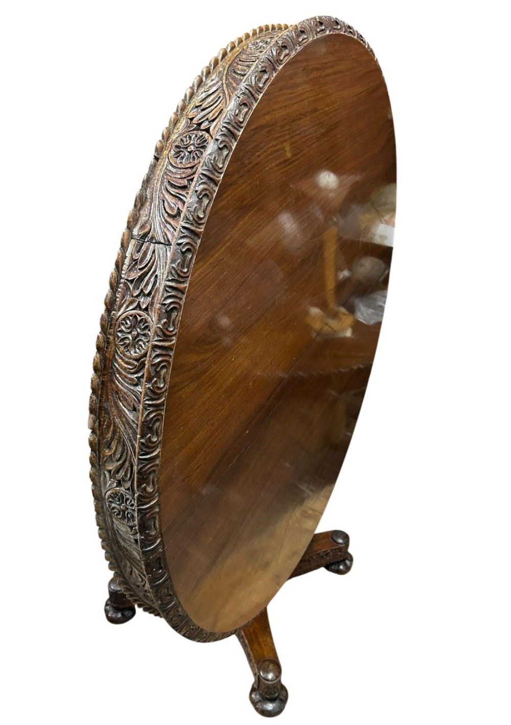 A round antique Burmese hardwood dining table featuring a polished top, an intricately carved apron, and a central pedestal base with tripod legs. View VIII