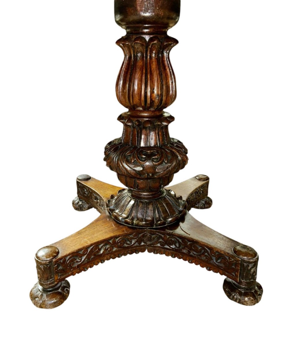 A round antique Burmese hardwood dining table featuring a polished top, an intricately carved apron, and a central pedestal base with tripod legs. View X