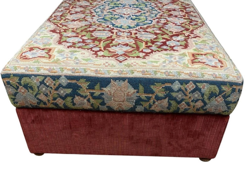 A low rectangular ottoman featuring a central multi-coloured floral needlepoint tapestry top bordered by red velvet side fabric with a pull tab. View IV