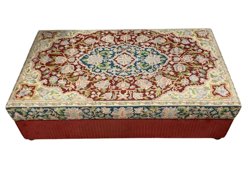 A low rectangular ottoman featuring a central multi-coloured floral needlepoint tapestry top bordered by red velvet side fabric with a pull tab. View V