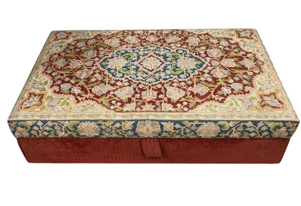 A low rectangular ottoman featuring a central multi-coloured floral needlepoint tapestry top bordered by red velvet side fabric with a pull tab. View IX