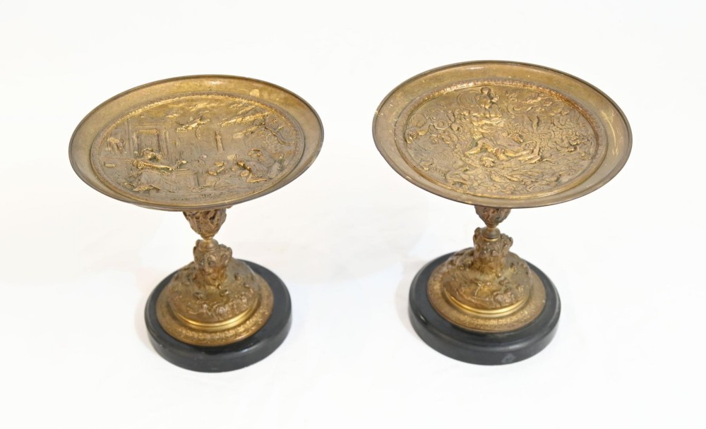 A pair of late 19th-century French ormolu classical tazzas with relief-cast circular dishes on decorative stems mounted on round black marble bases.