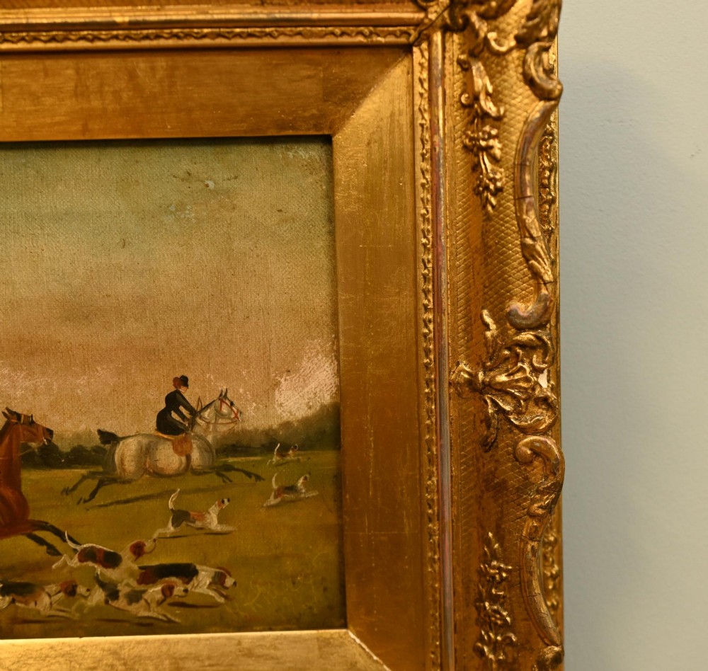 A pair of horizontal antique Victorian oil paintings in ornate gold gilt frames depicting horseback riders and hounds in a field. View VIII