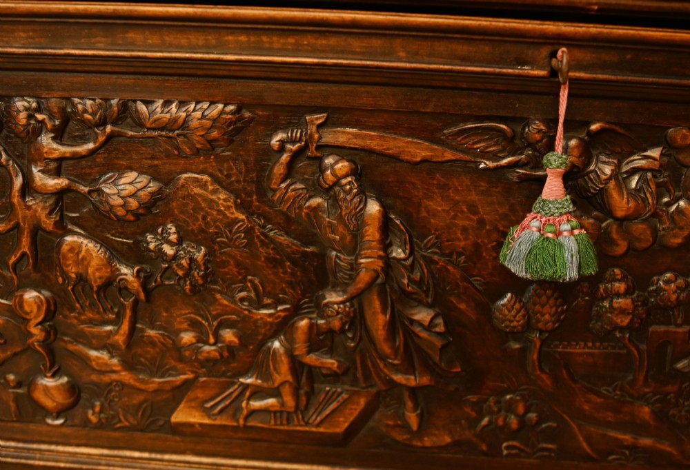 A carved dark walnut coffer featuring a central relief scene flanked by carved corner figures and decorative egg-and-dart base mouldings. View IV