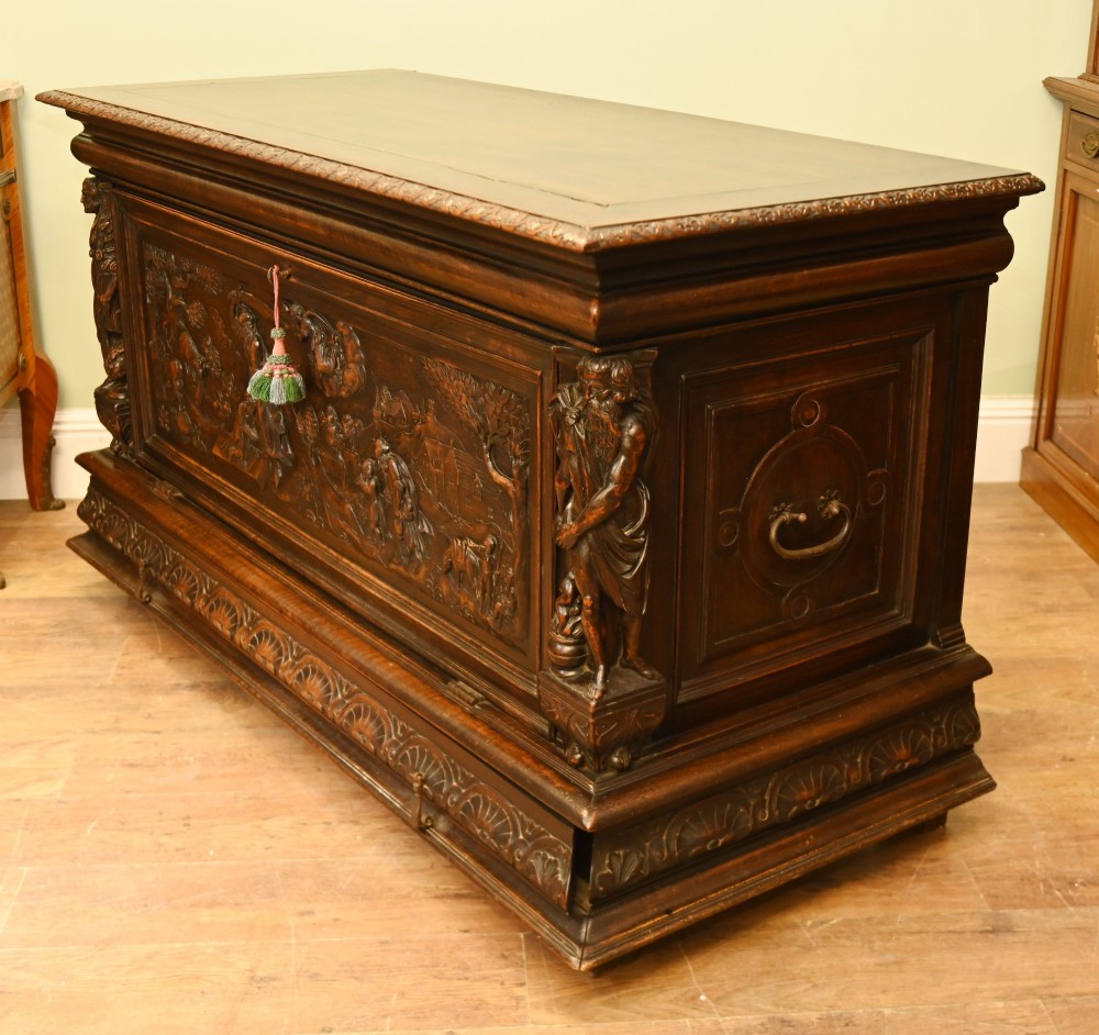 A carved dark walnut coffer featuring a central relief scene flanked by carved corner figures and decorative egg-and-dart base mouldings. View X