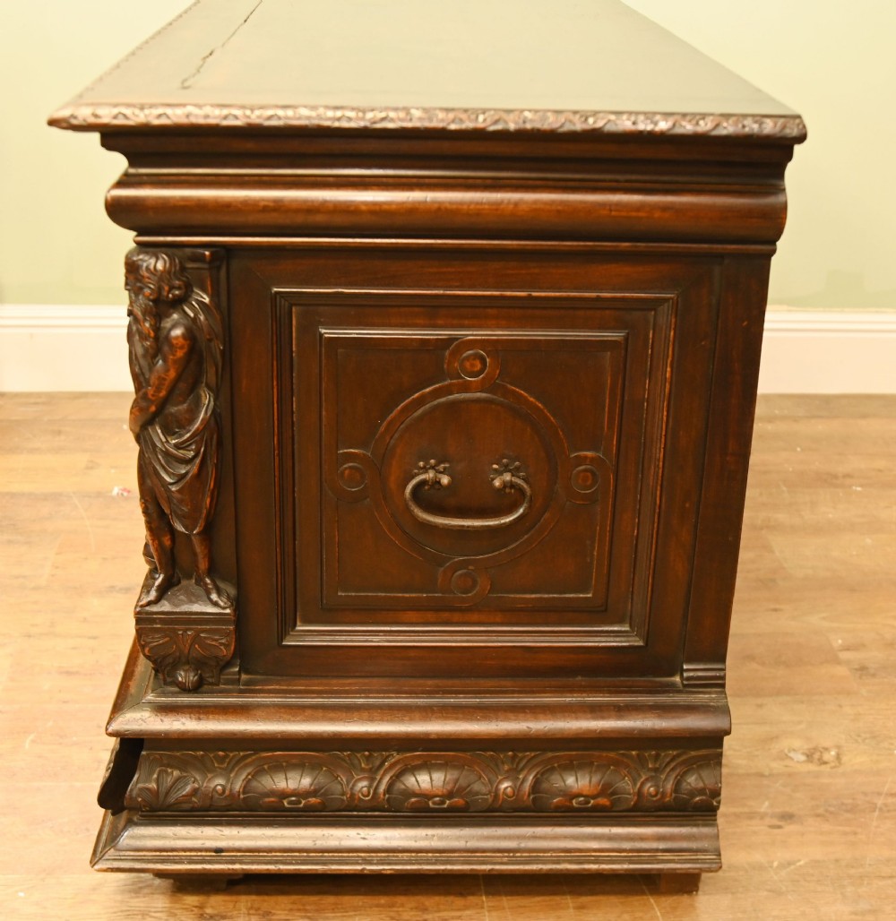 A carved dark walnut coffer featuring a central relief scene flanked by carved corner figures and decorative egg-and-dart base mouldings. View XII