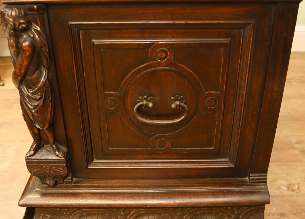 A carved dark walnut coffer featuring a central relief scene flanked by carved corner figures and decorative egg-and-dart base mouldings. View XIII