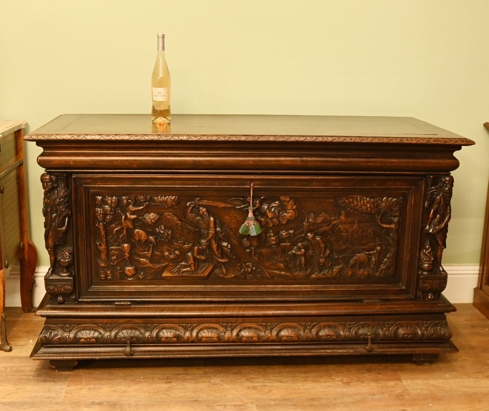 A carved dark walnut coffer featuring a central relief scene flanked by carved corner figures and decorative egg-and-dart base mouldings. View XV