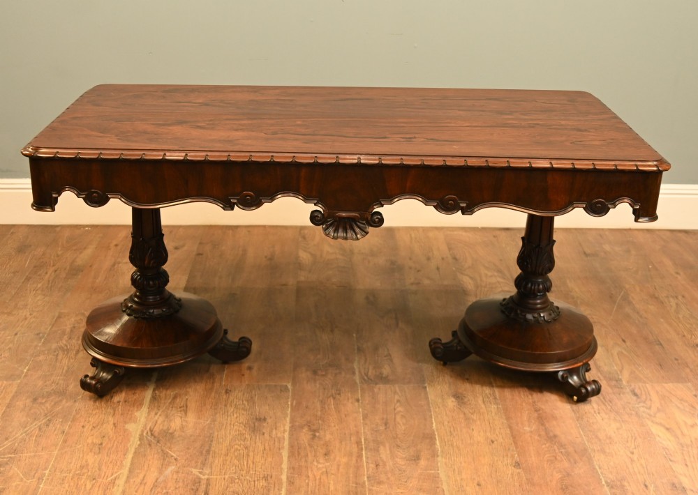 A William IV mahogany library table with a carved apron, shell detail, twin pedestal end supports, and scroll feet.