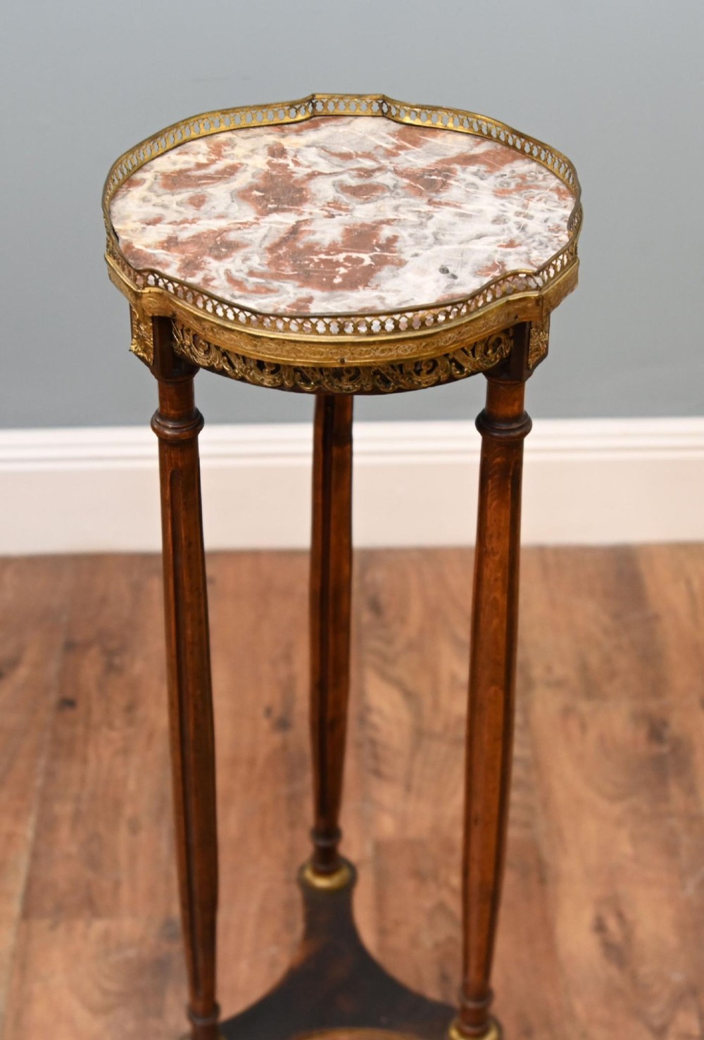A French Louis XVI style pedestal stand featuring a circular marble top with a pierced brass gallery, supported by three fluted legs and a lower tier.
