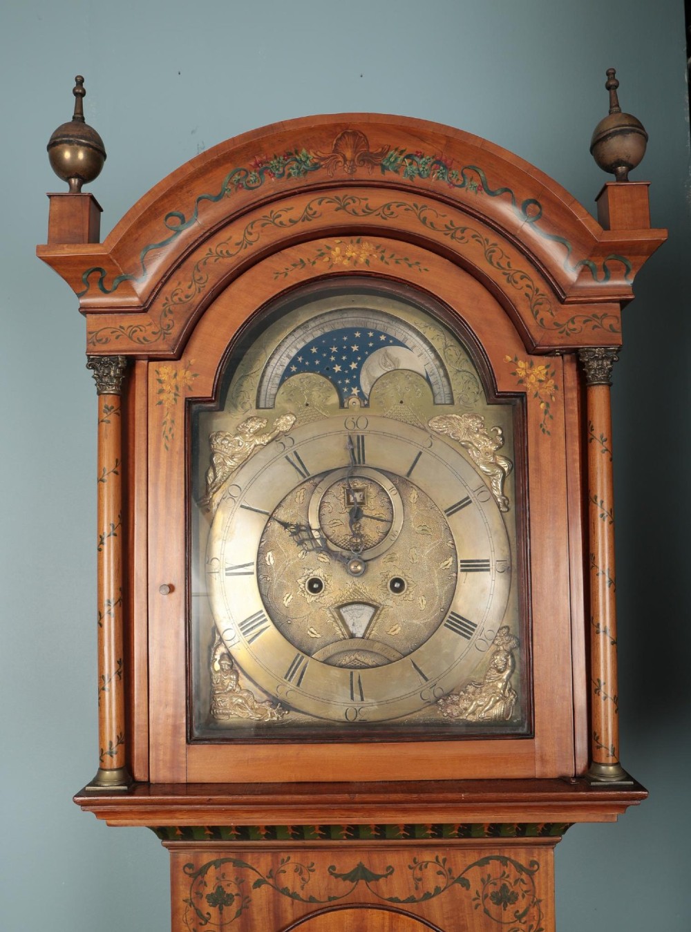An antique Scottish painted satinwood longcase clock with an arched moonphase dial, brass finials, and neoclassical floral painted panels. View VI