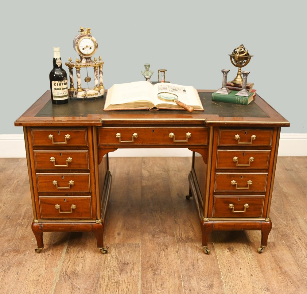 An antique French Empire mahogany kneehole desk featuring a green leather inset writing surface, nine drawers with brass handles, and brass castors. View II