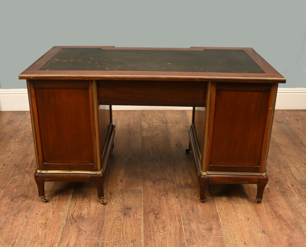 An antique French Empire mahogany kneehole desk featuring a green leather inset writing surface, nine drawers with brass handles, and brass castors. View III