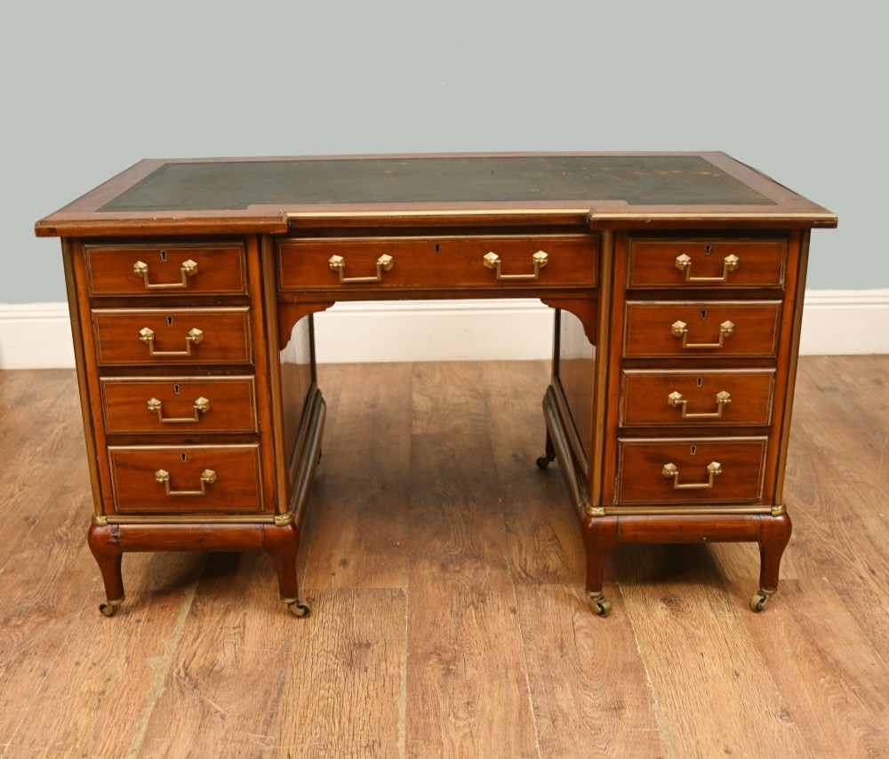 An antique French Empire mahogany kneehole desk featuring a green leather inset writing surface, nine drawers with brass handles, and brass castors.
