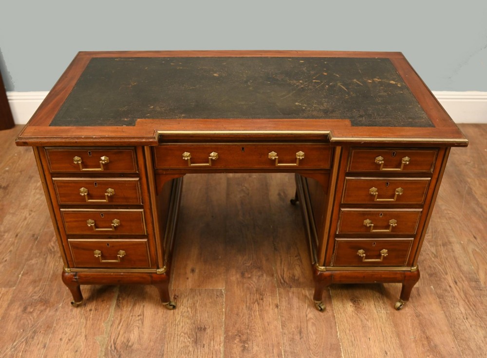 An antique French Empire mahogany kneehole desk featuring a green leather inset writing surface, nine drawers with brass handles, and brass castors. View IV