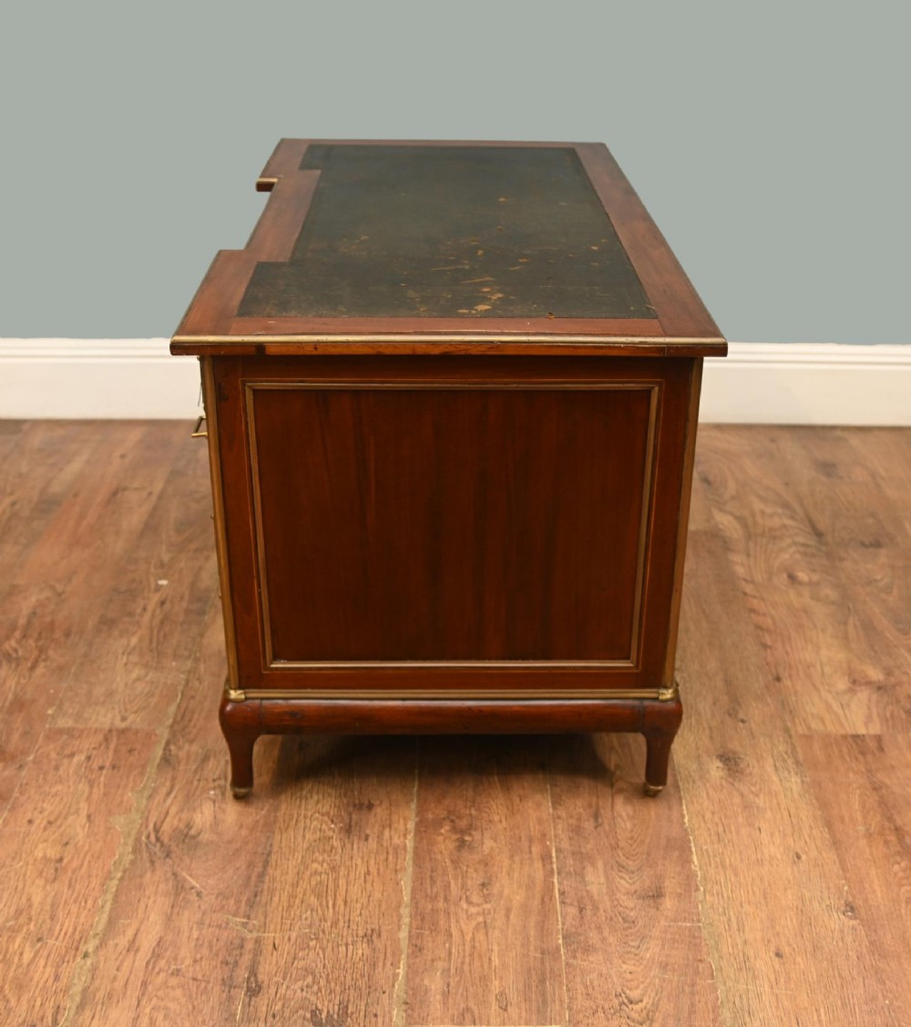 An antique French Empire mahogany kneehole desk featuring a green leather inset writing surface, nine drawers with brass handles, and brass castors. View V