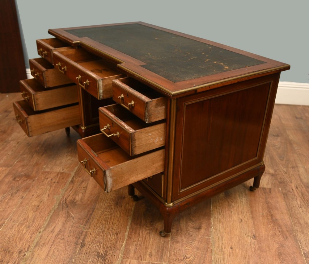 An antique French Empire mahogany kneehole desk featuring a green leather inset writing surface, nine drawers with brass handles, and brass castors. View VI