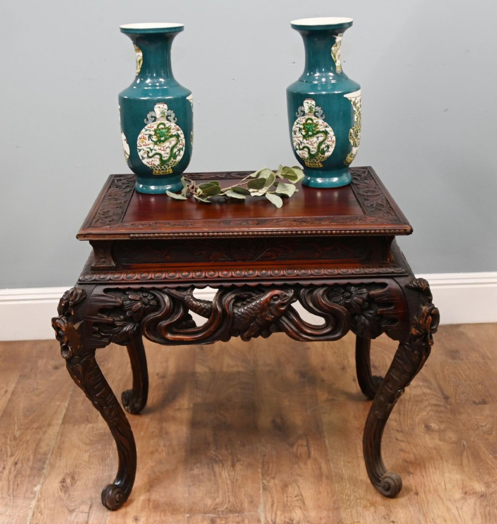 A dark brown antique Japanese side table featuring intricate relief carvings along the apron and cabriole legs.