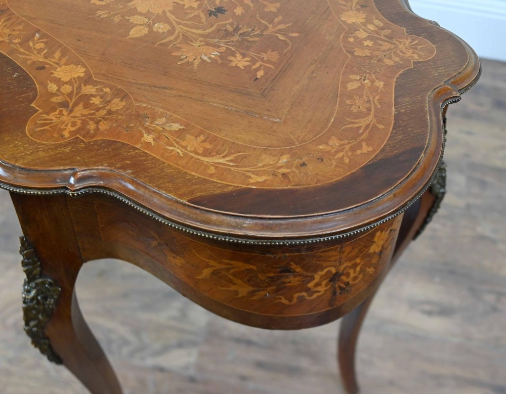 A French Rococo style writing table featuring a serpentine floral marquetry top, slender cabriole legs, and bronze mounts. View IV