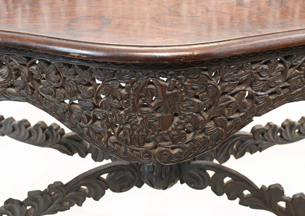 A late 19th-century Burmese dark teak console table featuring intricately pierced foliate carvings on the gallery back, skirt, and cross-stretcher, supported by legs carved as mythical figures. View II