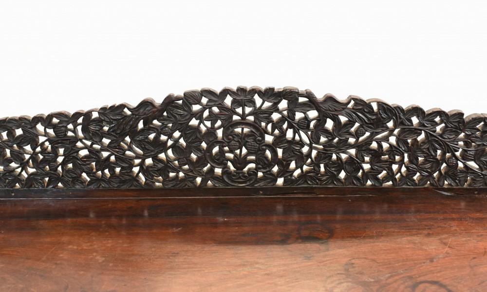 A late 19th-century Burmese dark teak console table featuring intricately pierced foliate carvings on the gallery back, skirt, and cross-stretcher, supported by legs carved as mythical figures. View IV