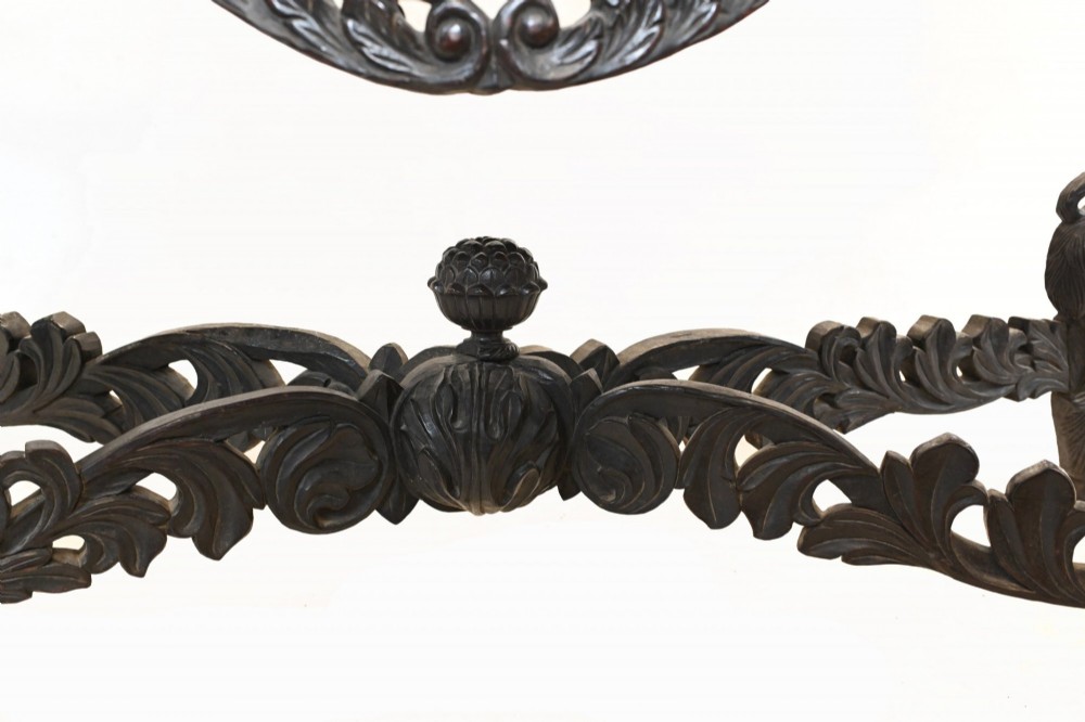 A late 19th-century Burmese dark teak console table featuring intricately pierced foliate carvings on the gallery back, skirt, and cross-stretcher, supported by legs carved as mythical figures. View V