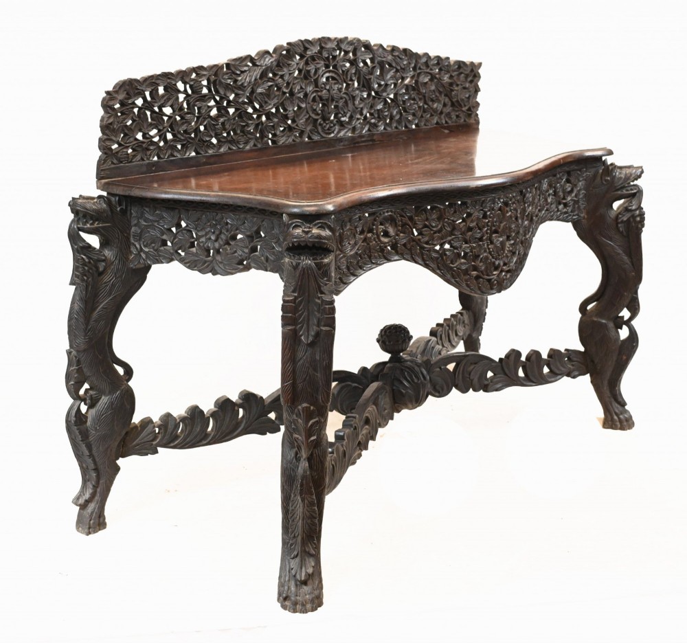 A late 19th-century Burmese dark teak console table featuring intricately pierced foliate carvings on the gallery back, skirt, and cross-stretcher, supported by legs carved as mythical figures. View VII