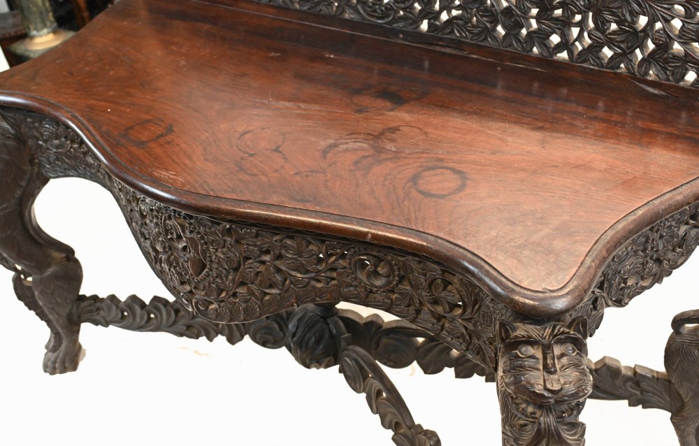 A late 19th-century Burmese dark teak console table featuring intricately pierced foliate carvings on the gallery back, skirt, and cross-stretcher, supported by legs carved as mythical figures. View VIII