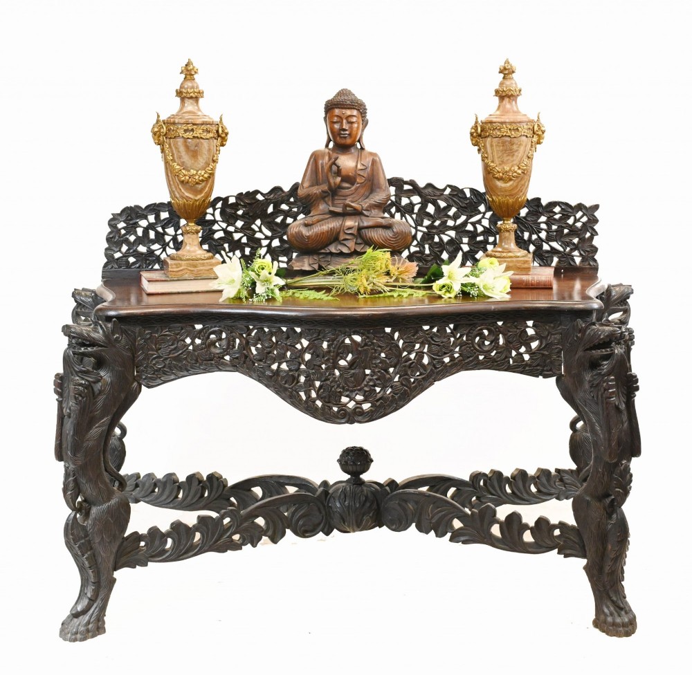 A late 19th-century Burmese dark teak console table featuring intricately pierced foliate carvings on the gallery back, skirt, and cross-stretcher, supported by legs carved as mythical figures. View X