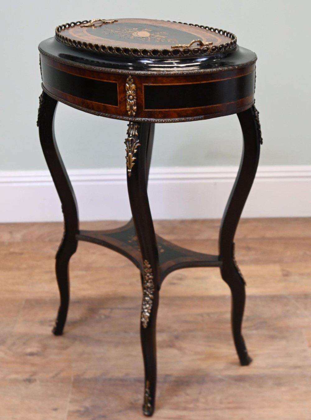 An antique French oval jardiniere table featuring amboyna wood veneer, floral marquetry, gilt-metal mounts, and ebonised cabriole legs. View II