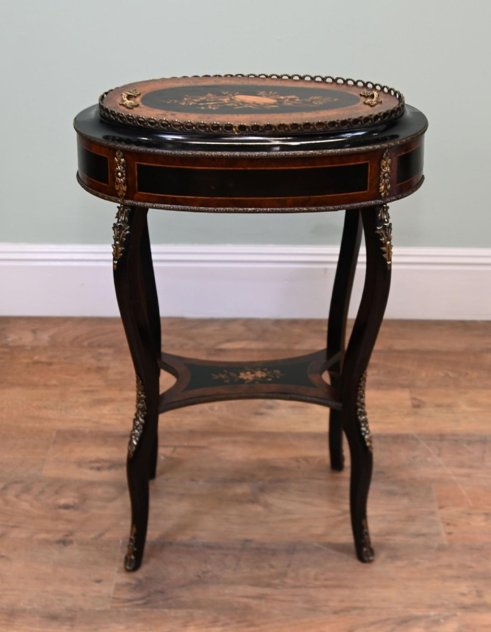 An antique French oval jardiniere table featuring amboyna wood veneer, floral marquetry, gilt-metal mounts, and ebonised cabriole legs. View VI
