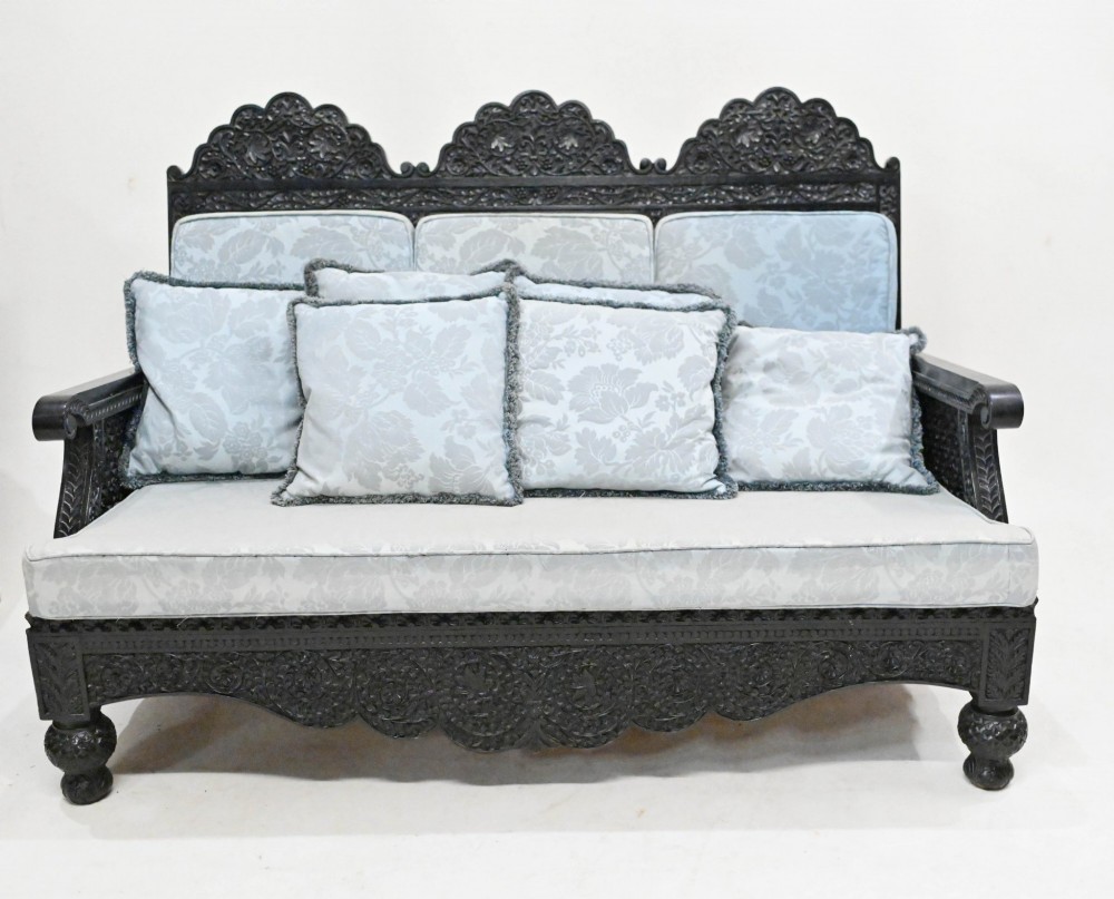 A dark hand-carved padauk wood suite featuring a long settee and four armchairs with pale blue upholstered cushions. View VII