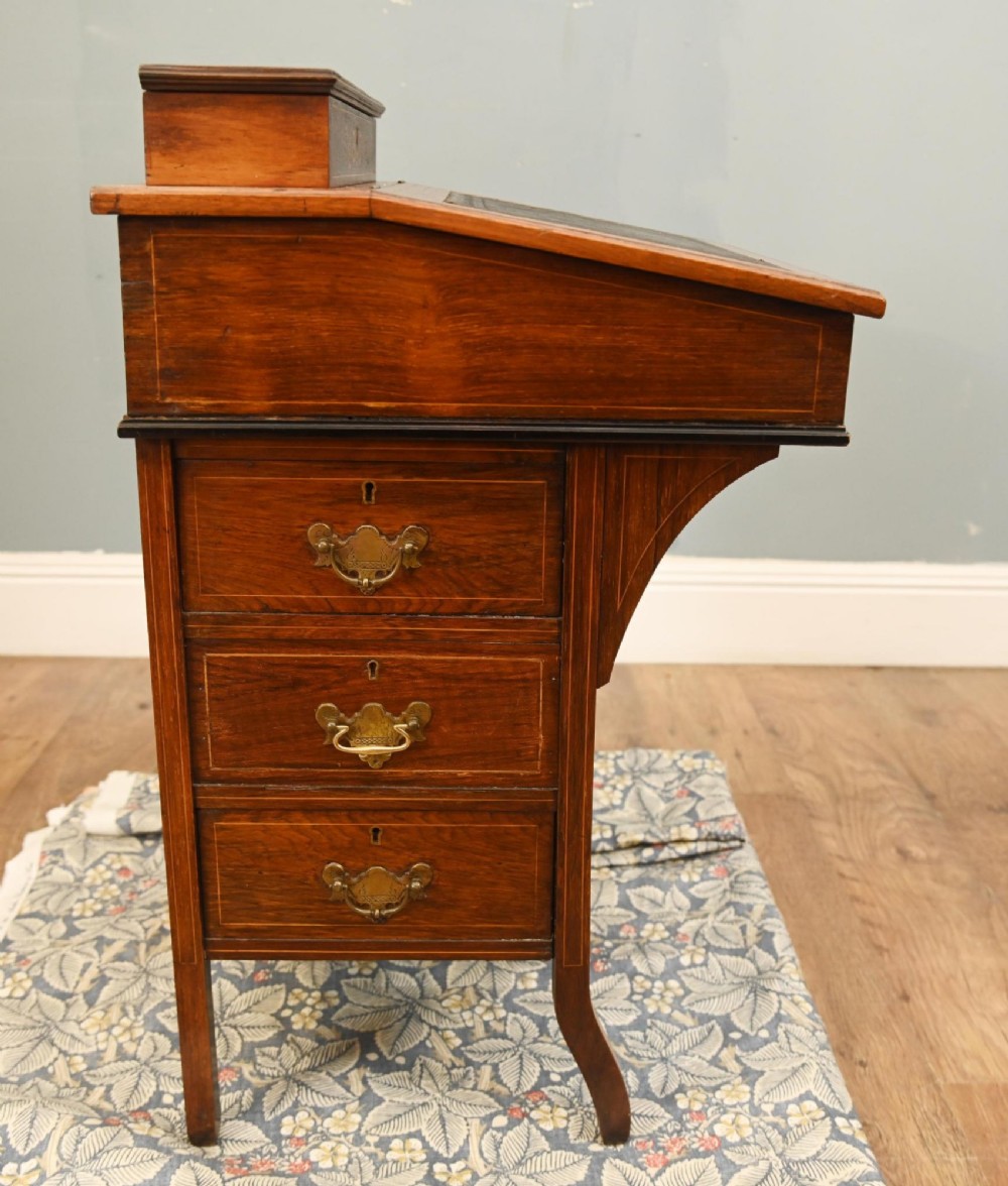 A late Victorian Sheraton Revival davenport desk crafted from warm brown wood, featuring decorative marquetry inlay and a dark leather inset writing surface. View X