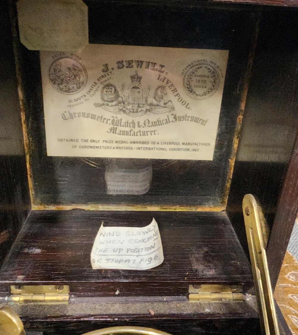 A Victorian brass marine chronometer mounted inside a brass-bound dark mahogany box with a printed manufacturer label. View XIII