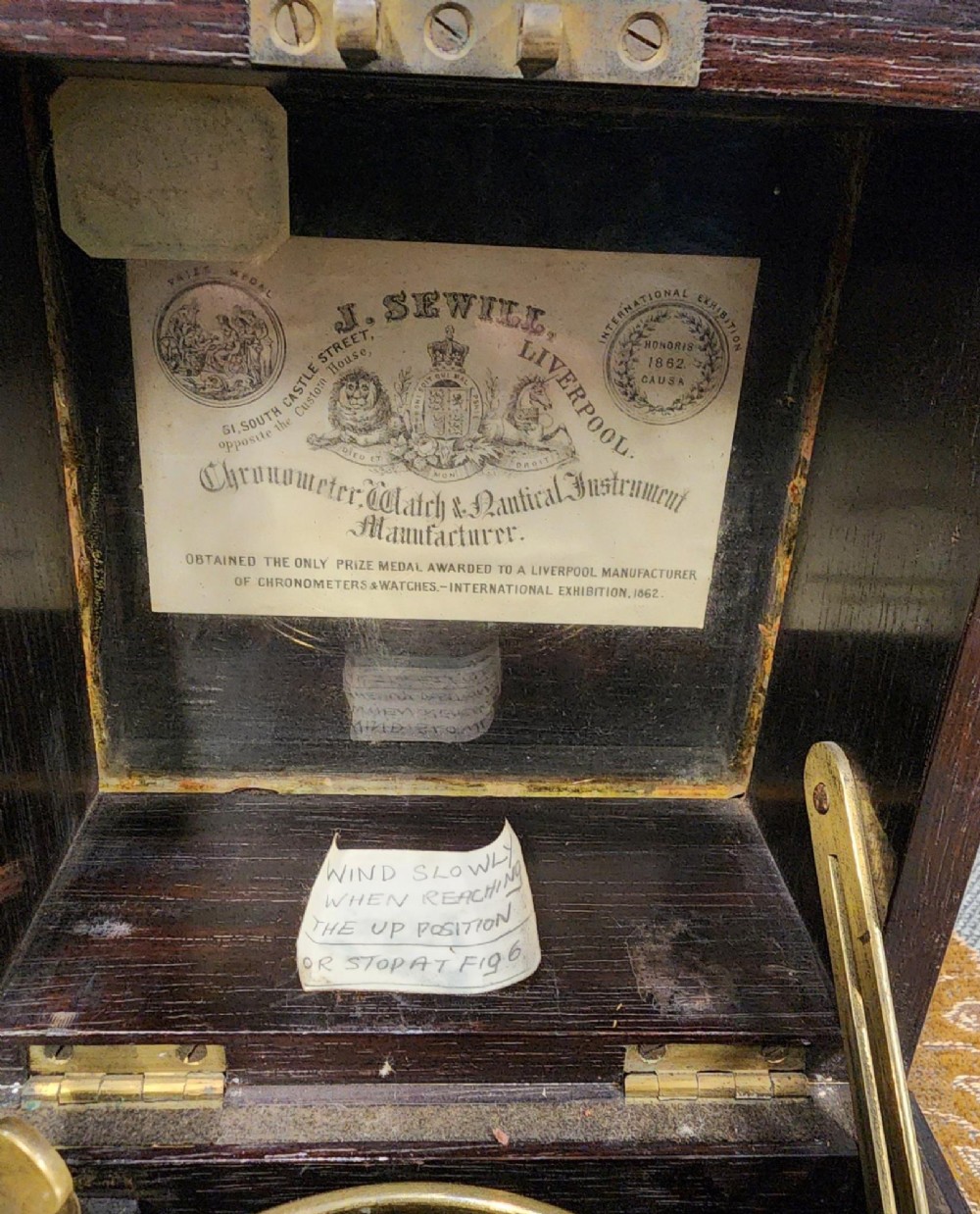 A Victorian brass marine chronometer mounted inside a brass-bound dark mahogany box with a printed manufacturer label. View XIV