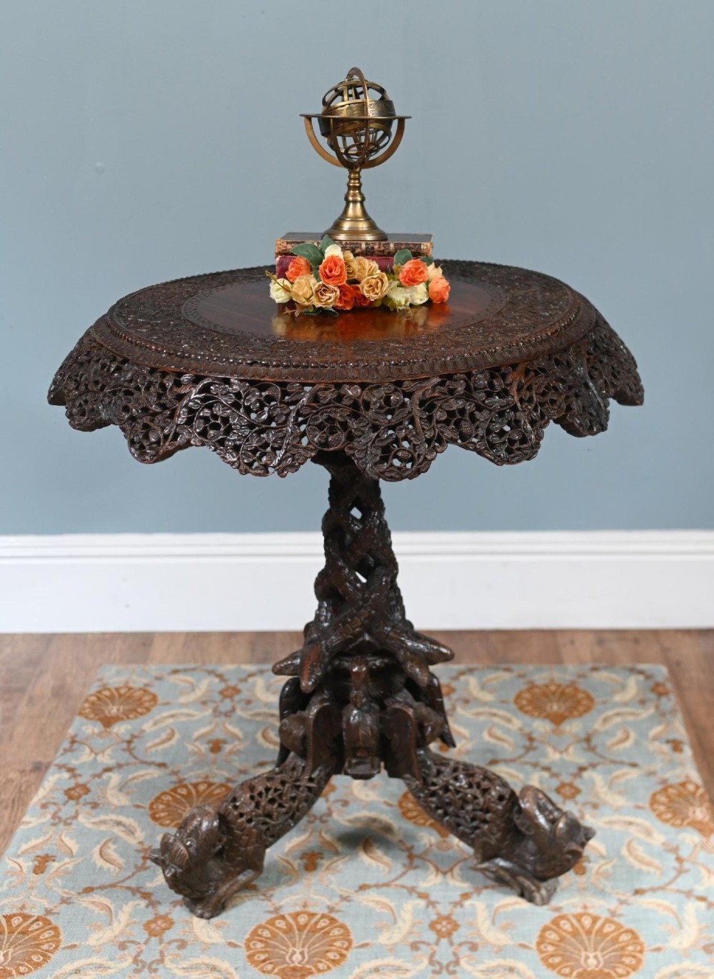 An antique dark hardwood Burmese side table with intricate pierced foliage carving around the circular top and a carved tripod base featuring mythological figure feet.