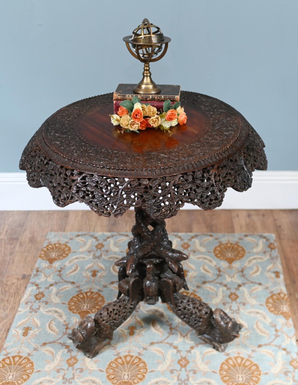 An antique dark hardwood Burmese side table with intricate pierced foliage carving around the circular top and a carved tripod base featuring mythological figure feet. View II