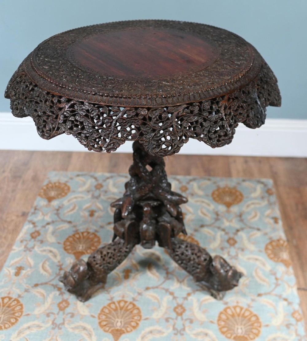 An antique dark hardwood Burmese side table with intricate pierced foliage carving around the circular top and a carved tripod base featuring mythological figure feet. View III
