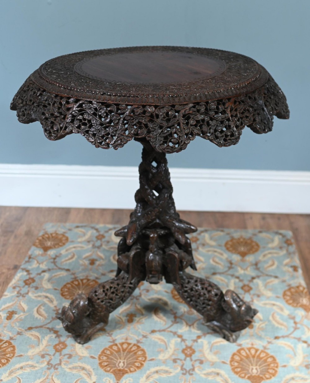 An antique dark hardwood Burmese side table with intricate pierced foliage carving around the circular top and a carved tripod base featuring mythological figure feet. View IV