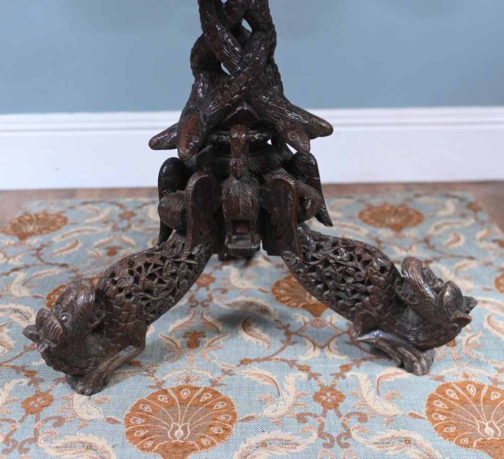 An antique dark hardwood Burmese side table with intricate pierced foliage carving around the circular top and a carved tripod base featuring mythological figure feet. View VII