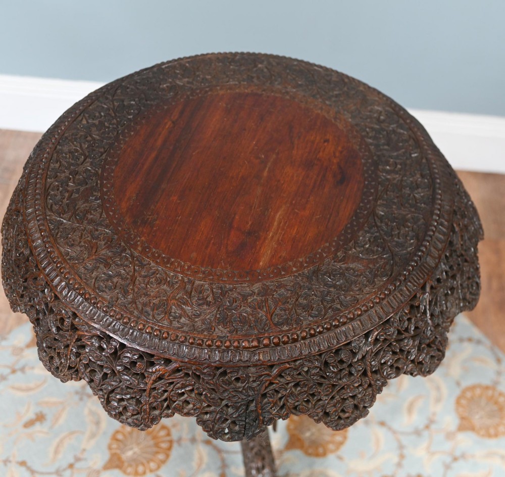 An antique dark hardwood Burmese side table with intricate pierced foliage carving around the circular top and a carved tripod base featuring mythological figure feet. View XII
