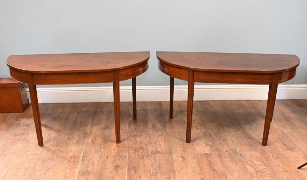A pair of antique Georgian mahogany demi-lune console tables with semi-circular tops and straight tapered legs.