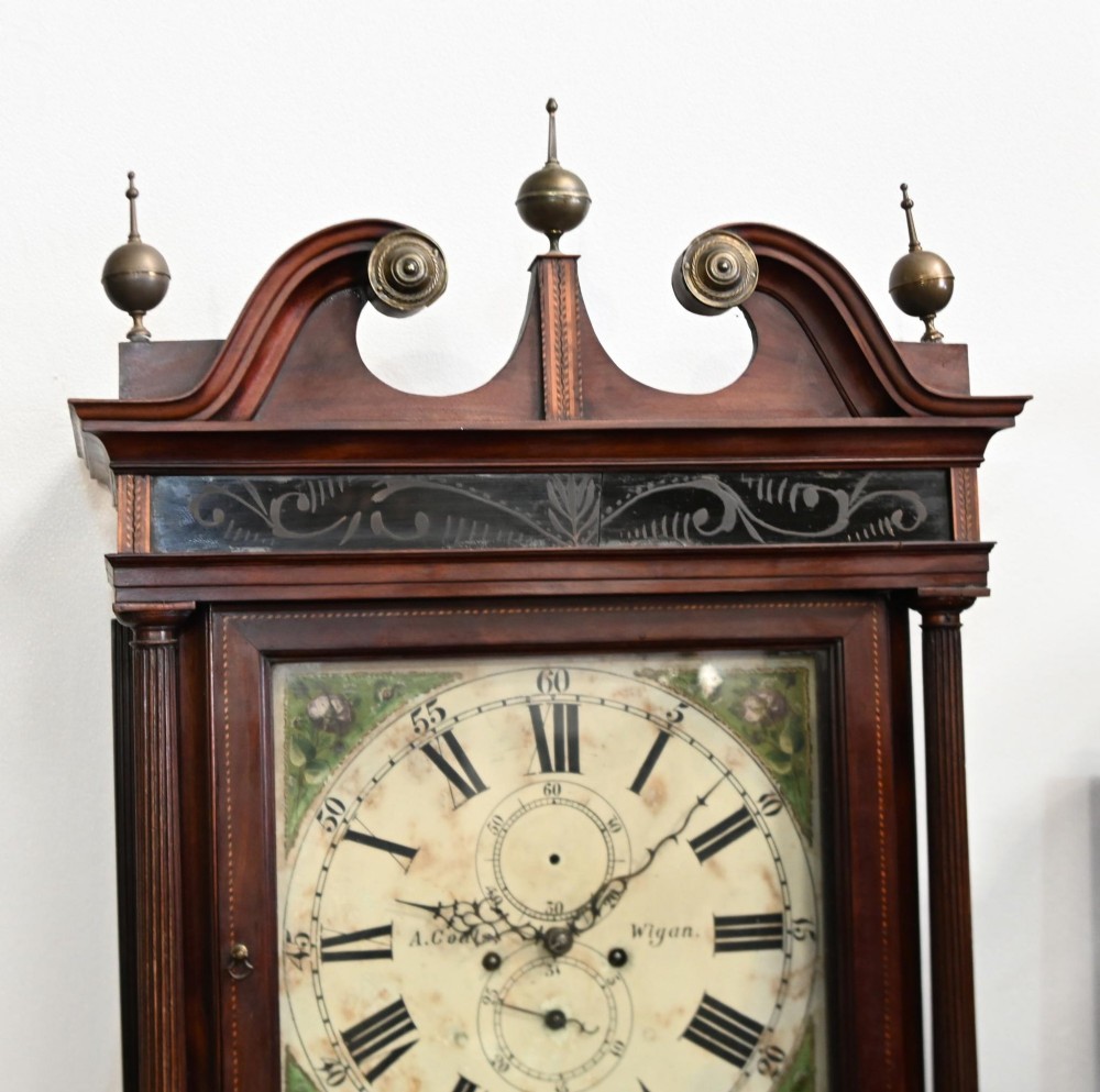 A Georgian mahogany longcase clock featuring a swan-neck pediment with three brass finials, a painted dial with Roman numerals, and a flame mahogany door. View II