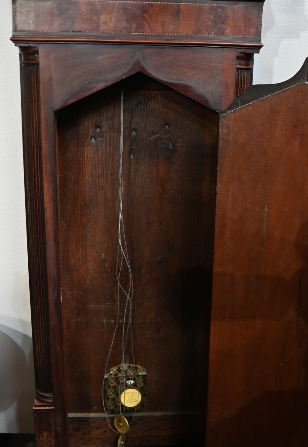 A Georgian mahogany longcase clock featuring a swan-neck pediment with three brass finials, a painted dial with Roman numerals, and a flame mahogany door. View V