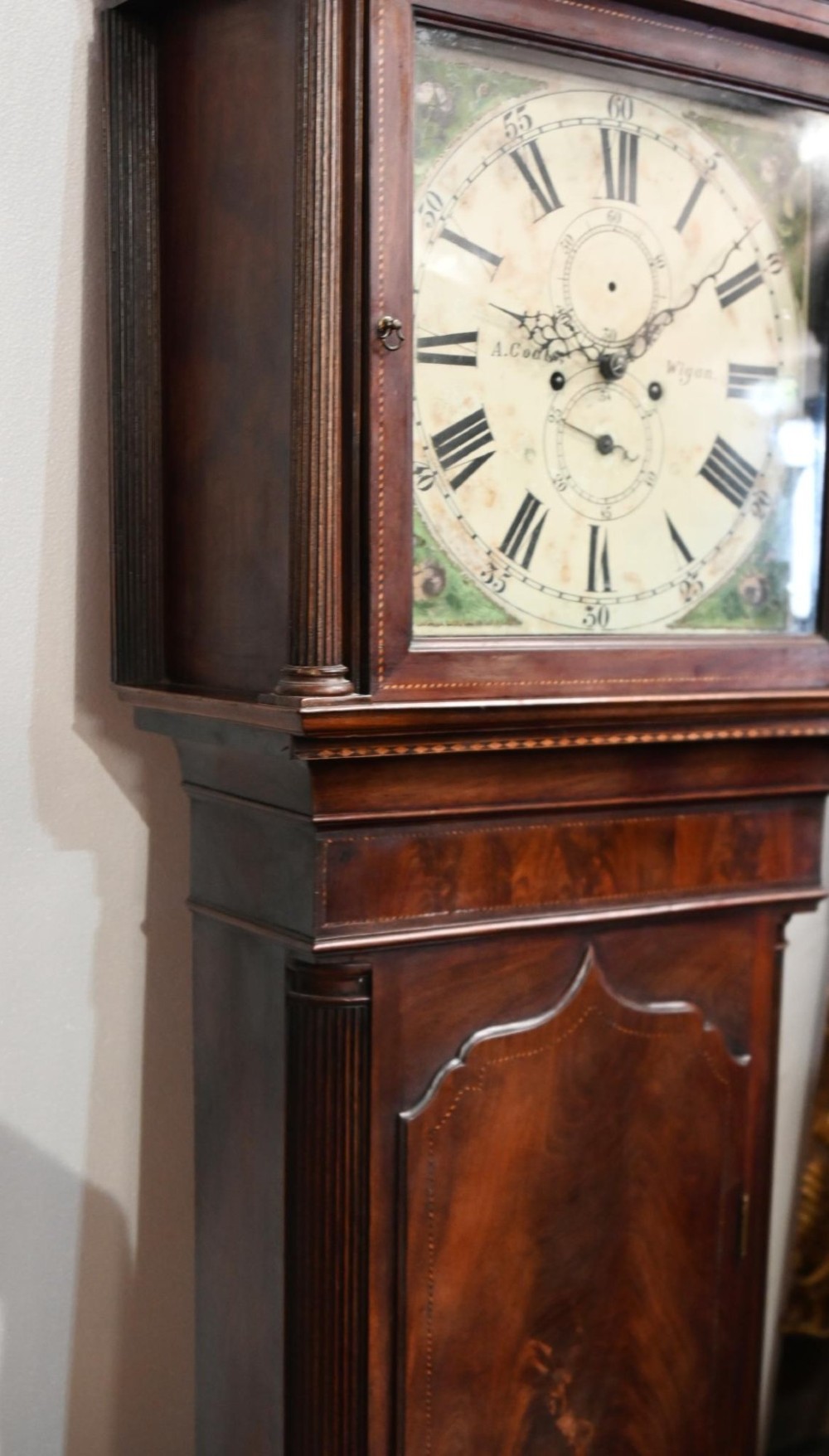 A Georgian mahogany longcase clock featuring a swan-neck pediment with three brass finials, a painted dial with Roman numerals, and a flame mahogany door. View VII