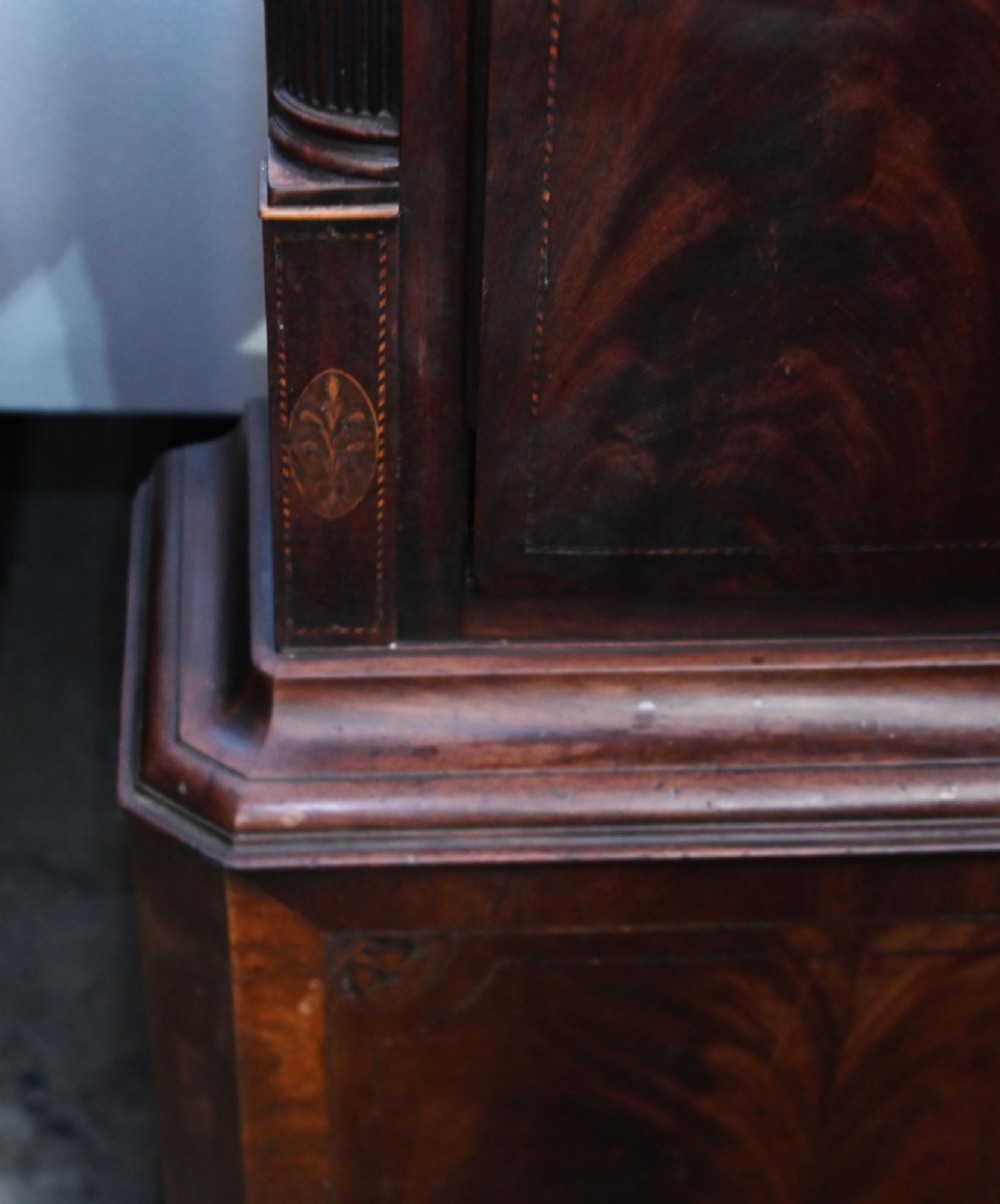A Georgian mahogany longcase clock featuring a swan-neck pediment with three brass finials, a painted dial with Roman numerals, and a flame mahogany door. View VIII