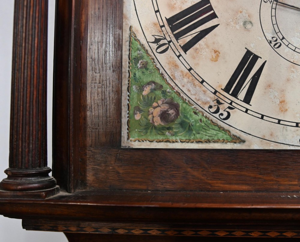 A Georgian mahogany longcase clock featuring a swan-neck pediment with three brass finials, a painted dial with Roman numerals, and a flame mahogany door. View XI